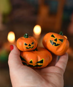 Bumbu set of 3 Halloween pumpkins held in an adult's hand to show scale. A Grimm's celebration ring with lit candles can be seen in the background. These wooden figures are part of a wide range of expertly hand crafted wooden toys here at Babipur. 