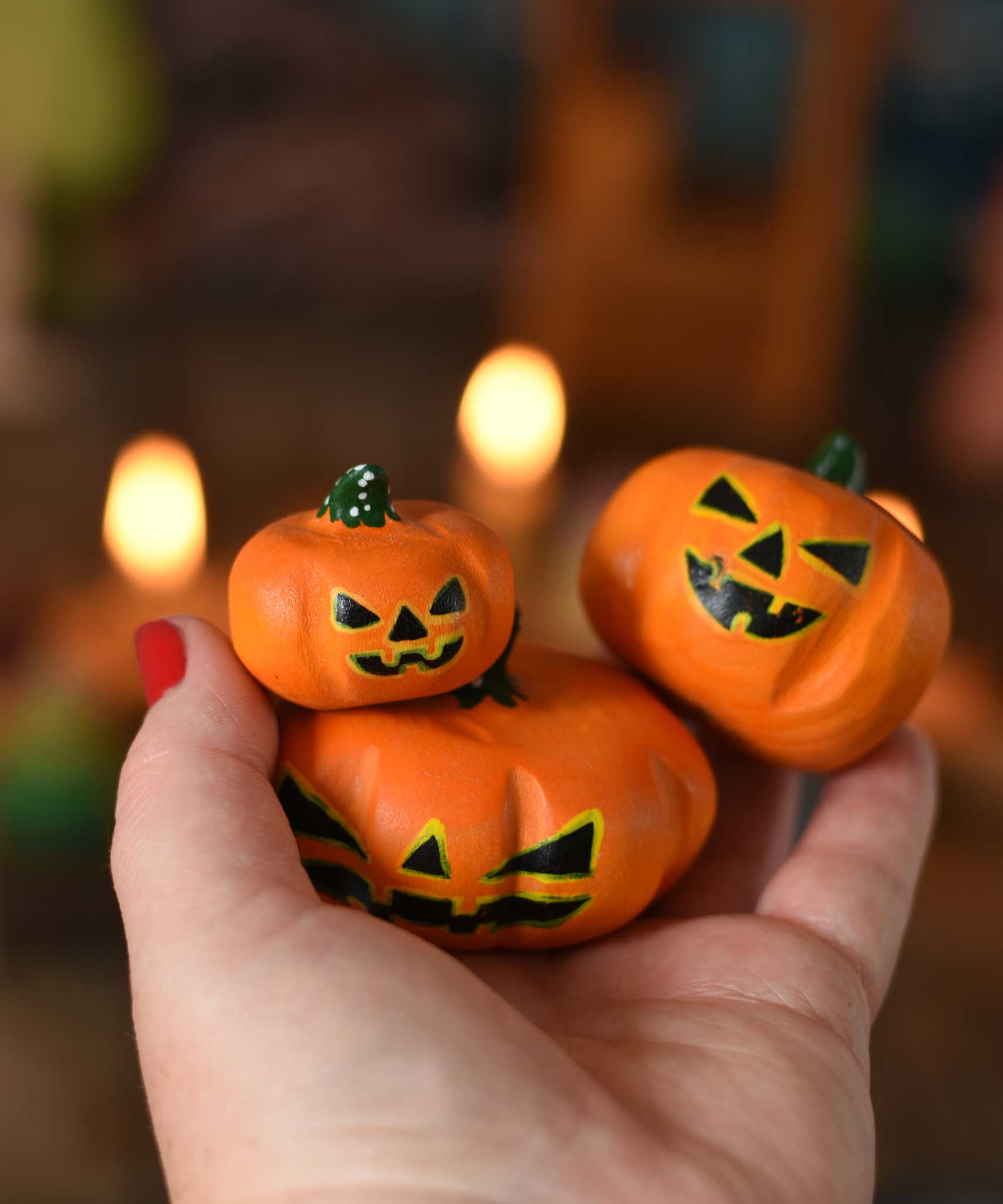 Bumbu set of 3 Halloween pumpkins held in an adult's hand to show scale. A Grimm's celebration ring with lit candles can be seen in the background. These wooden figures are part of a wide range of expertly hand crafted wooden toys here at Babipur. 
