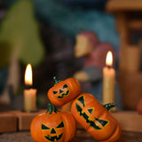 A collection of three Bumbu Halloween pumpkins placed at the front of a seasonal display scene. A Grimm's celebration ring with lit candles can be seen in the background. These wooden figures are part of a wide range of expertly hand crafted wooden toys here at Babipur. 