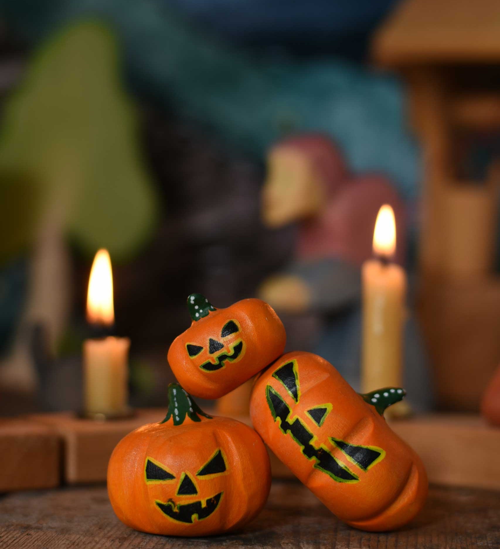 A collection of three Bumbu Halloween pumpkins placed at the front of a seasonal display scene. A Grimm's celebration ring with lit candles can be seen in the background. These wooden figures are part of a wide range of expertly hand crafted wooden toys here at Babipur. 