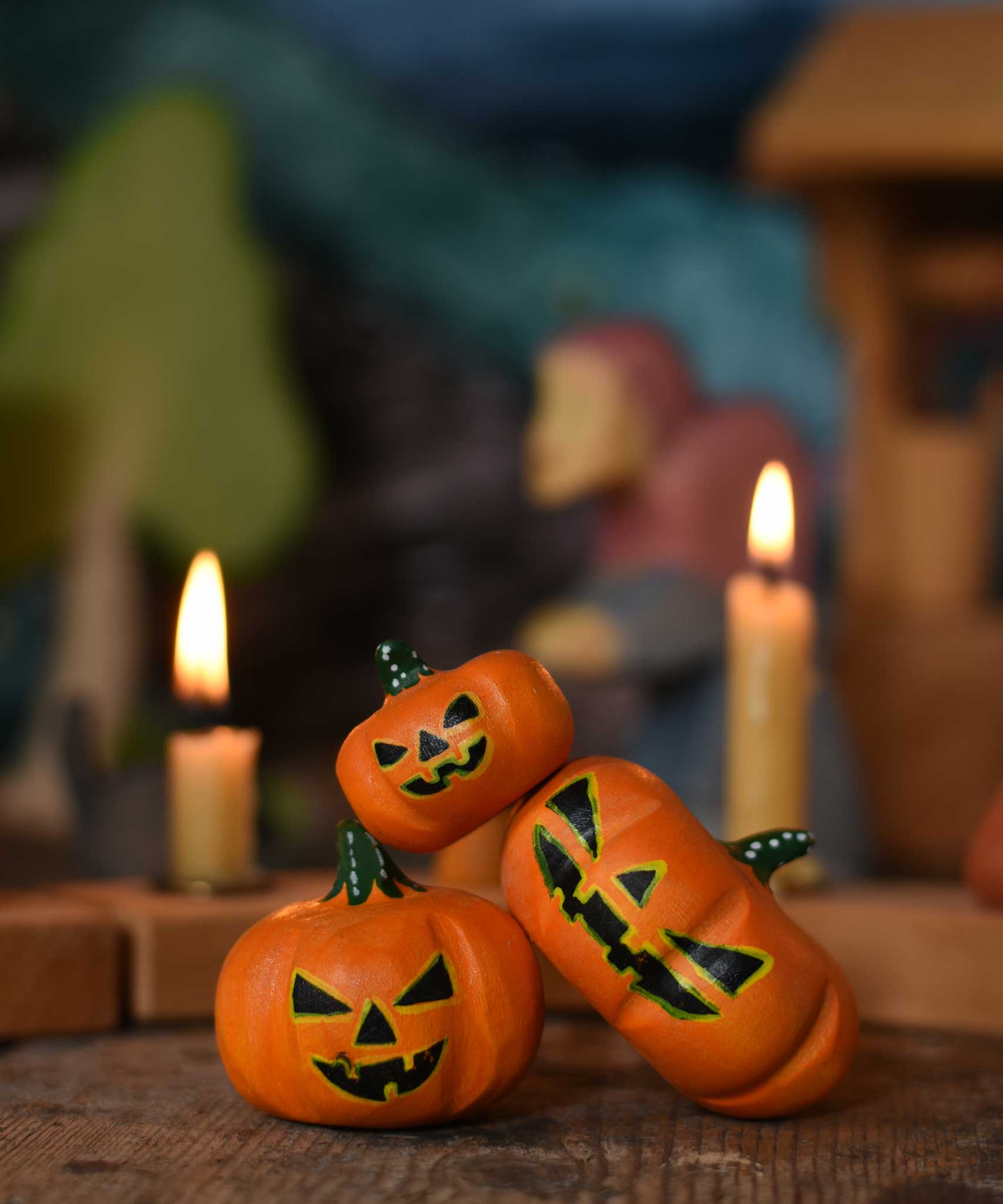 A collection of three Bumbu Halloween pumpkins placed at the front of a seasonal display scene. A Grimm's celebration ring with lit candles can be seen in the background. These wooden figures are part of a wide range of expertly hand crafted wooden toys here at Babipur. 