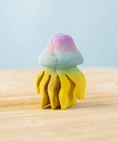The Bumbu hand carved wooden jellyfish toy. It is has a rounded bell-shape head which is hand painted in ombre pink and blue, with bright yellow tentacles. 