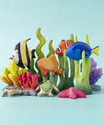 An imaginative play scene with an underwater theme, made up of hand carved Bumbu wooden toys, such as seaweed, goldfish, royal blue fish, and clownfish.