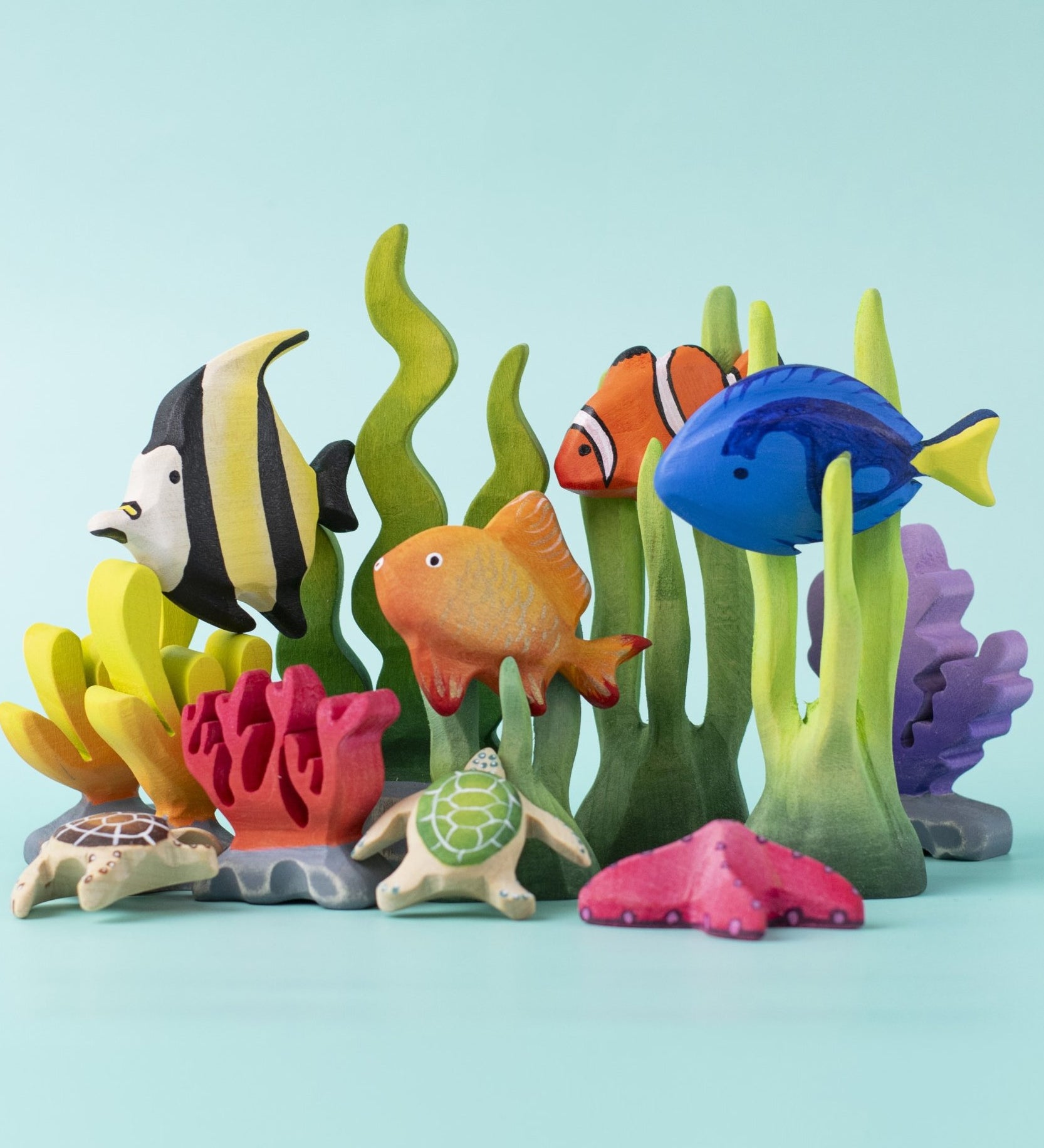 An imaginative play scene with an underwater theme, made up of hand carved Bumbu wooden toys, such as seaweed, goldfish, royal blue fish, and clownfish.