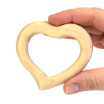 Hand holding the Bumbu handmade wooden baby teething toy heart in front of a white background