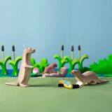 Bumbu otter and curious otter toys on a green floor in front of some Bumbu cattail plants and a blue background