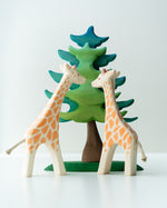 2 Ostheimer giraffe figures stood on a white background next to a Bumbu plastic-free spruce tree toy