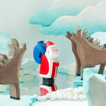 Bumbu plastic-free Father Christmas figure stood on a mirror next to some Bumbu stags and a winter Maple tree toy