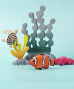 The Bumbu handmade wooden clownfish toy, in an imaginative underwater play scene along with Bumbu wooden seaweed, kelp, starfish, and turtle. 