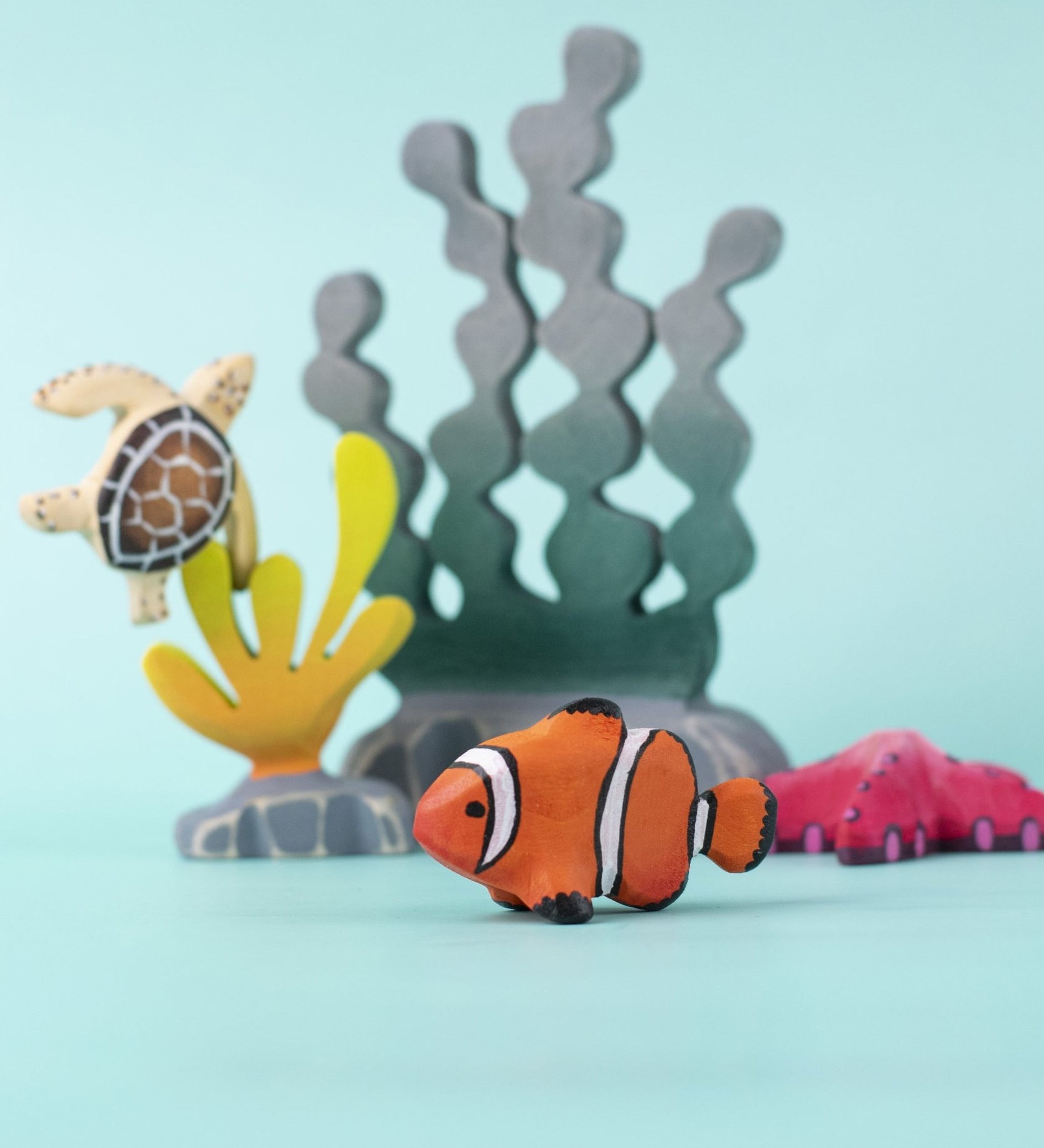 The Bumbu handmade wooden clownfish toy, in an imaginative underwater play scene along with Bumbu wooden seaweed, kelp, starfish, and turtle. 