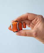 A hand holding the Bumbu hand painted wooden clownfish toy figure, for size reference