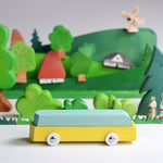 Bumbu waldorf car toy on a white table in front of a green wooden landscape scene