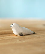Bumbu Toys harp seal pup handmade wooden toy figure placed on a wooden surface.