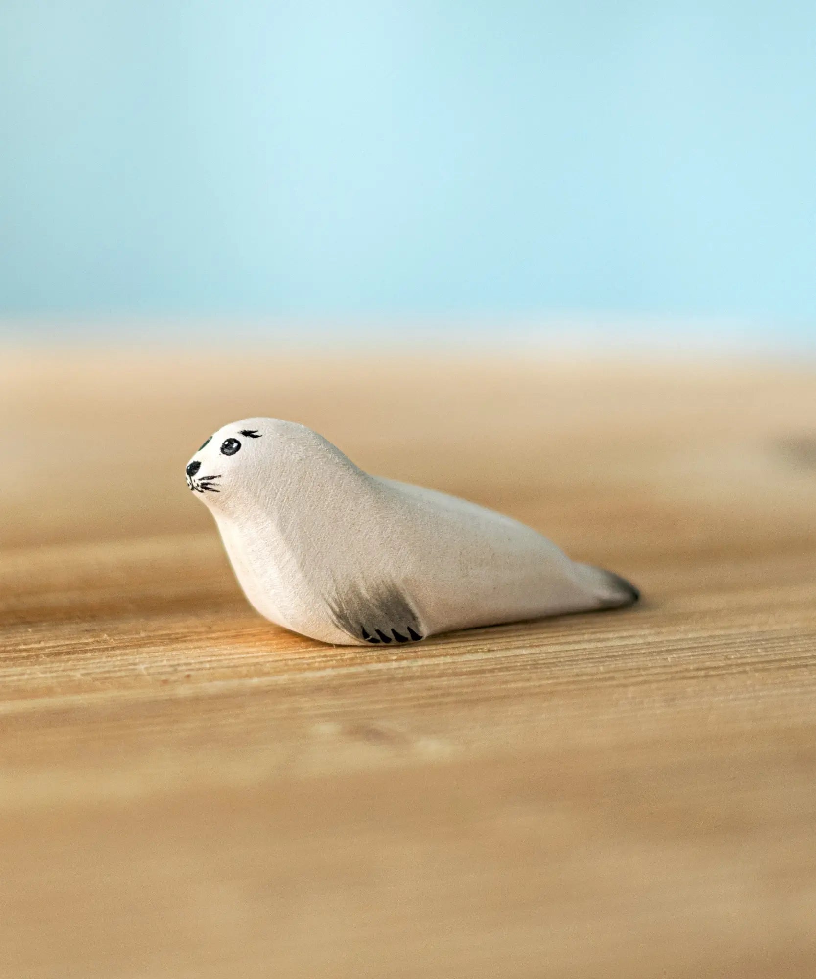 Bumbu Toys harp seal pup handmade wooden toy figure placed on a wooden surface.