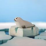 Bumbu Toys harp seal pup handmade wooden toy figure placed on an ice berg piece in a small world play scene.