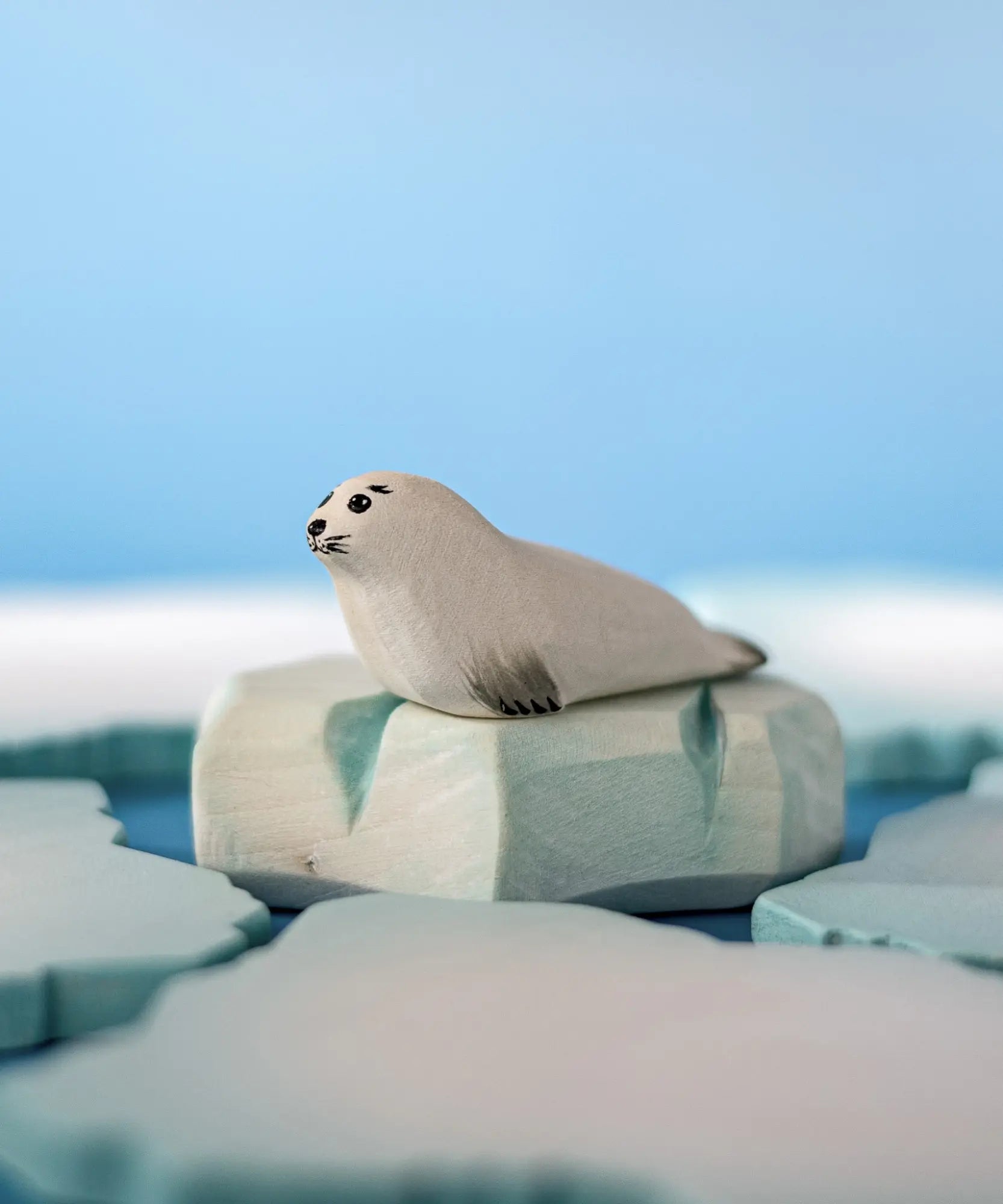 Bumbu Toys harp seal pup handmade wooden toy figure placed on an ice berg piece in a small world play scene.