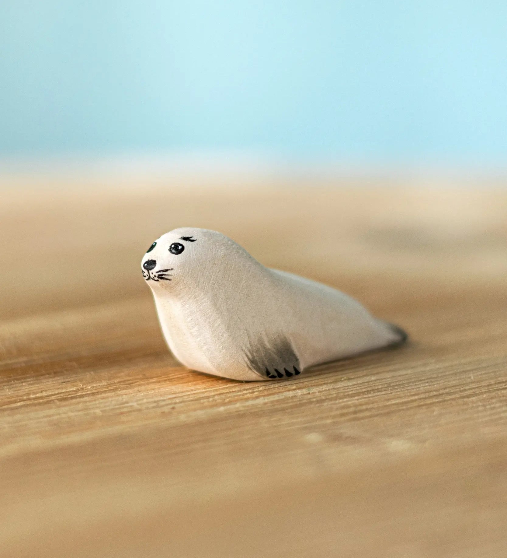 Bumbu Toys harp seal pup handmade wooden toy figure placed on a wooden surface.