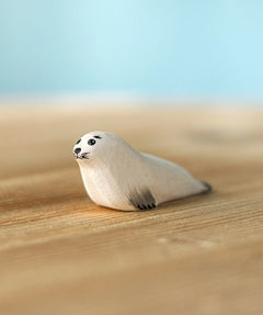 Bumbu Toys harp seal pup handmade wooden toy figure placed on a wooden surface.