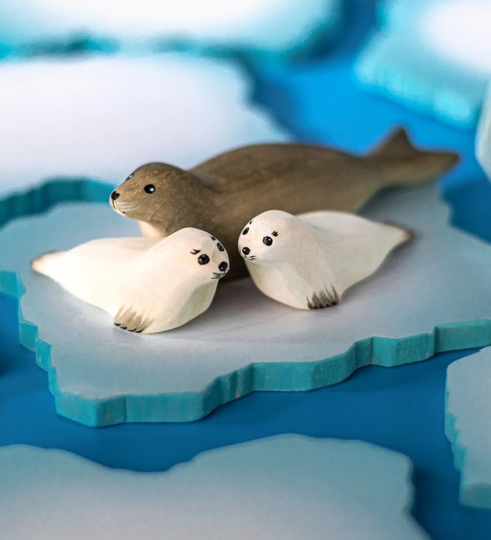 Two Bumbu Toys harp seal pups handmade wooden toy figures placed on an ice flow with an adult harp seal.