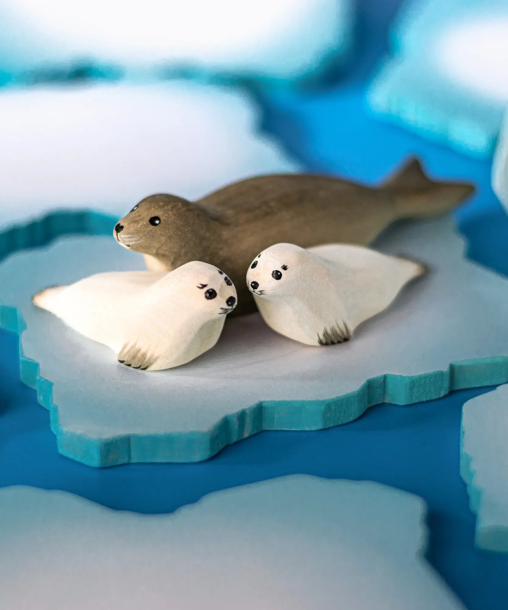 Two Bumbu Toys harp seal pups handmade wooden toy figures placed on an ice flow with an adult harp seal.