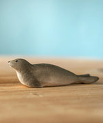 Bumbu harp seal handmade wooden toy figure placed on a wooden surface.