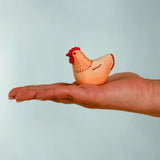 Adult hand holding the Bumbu handcrafted wooden brown hen decorative figure showing size