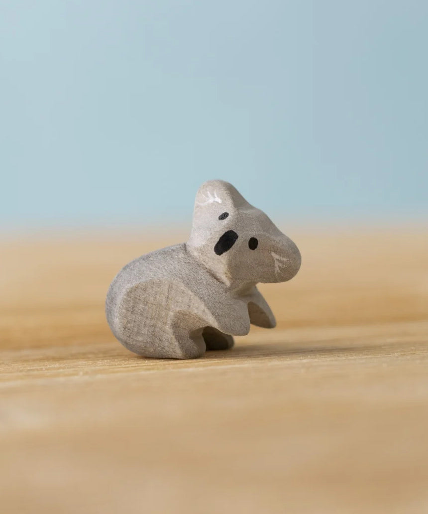 A Bumbu Toys handmade wooden Koala Cub figure placed on a wooden surface.