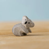 A Bumbu Toys handmade wooden Koala Cub figure placed on a wooden surface.