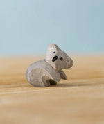 A Bumbu Toys handmade wooden Koala Cub figure placed on a wooden surface.