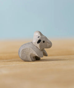 A Bumbu Toys handmade wooden Koala Cub figure placed on a wooden surface.