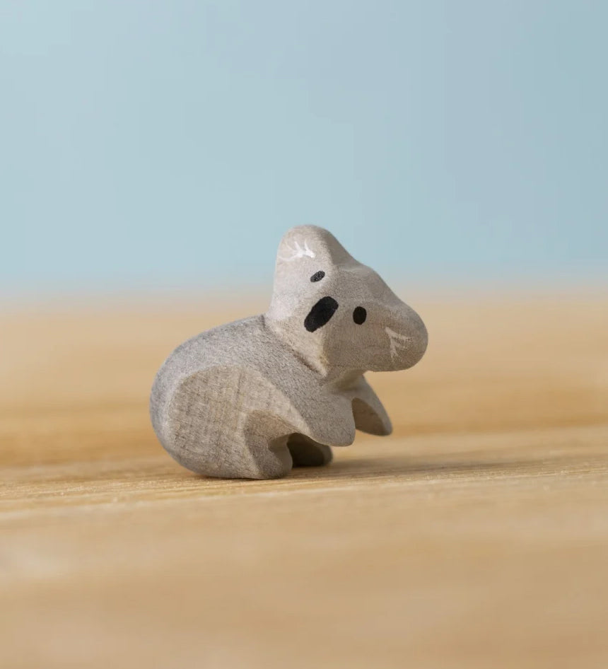A Bumbu Toys handmade wooden Koala Cub figure placed on a wooden surface.