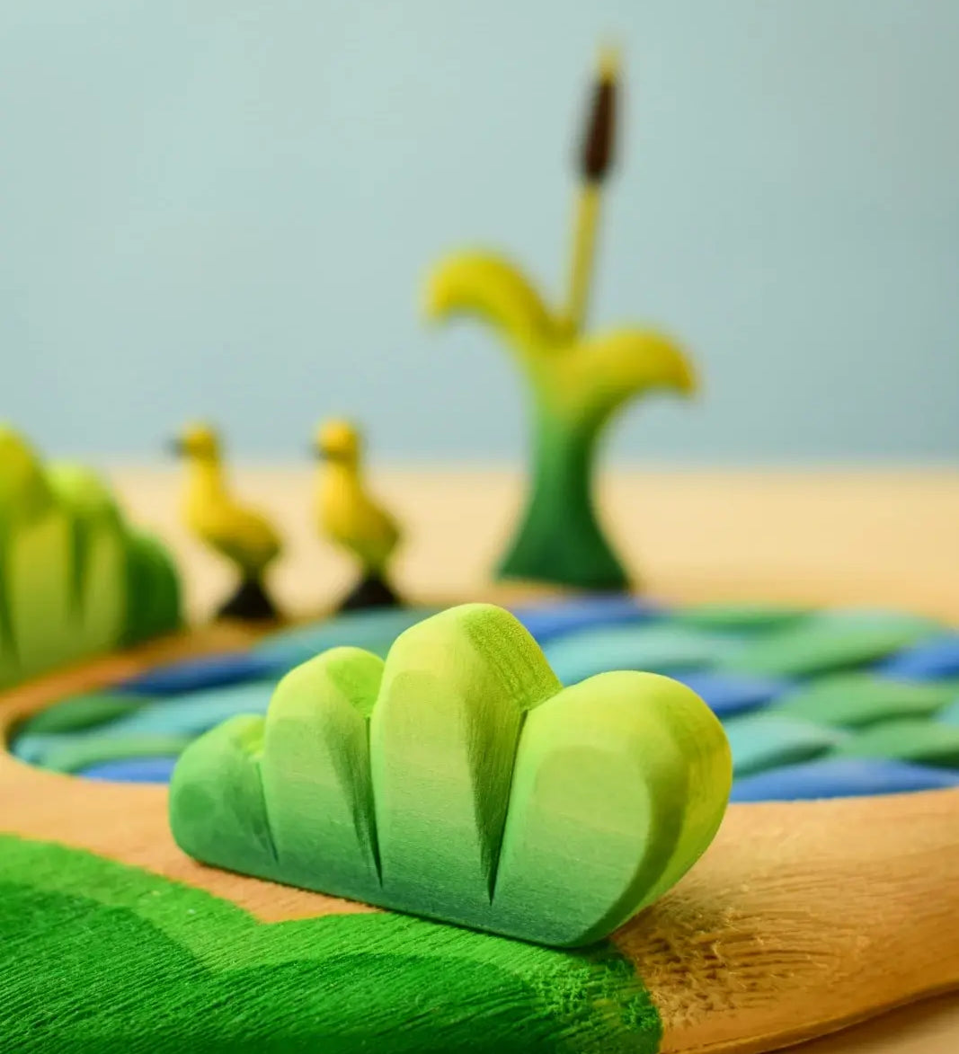 Bumbu Toys lake bush wooden toy scenery piece placed in a small world play scene with a lake and ducklings in the background.