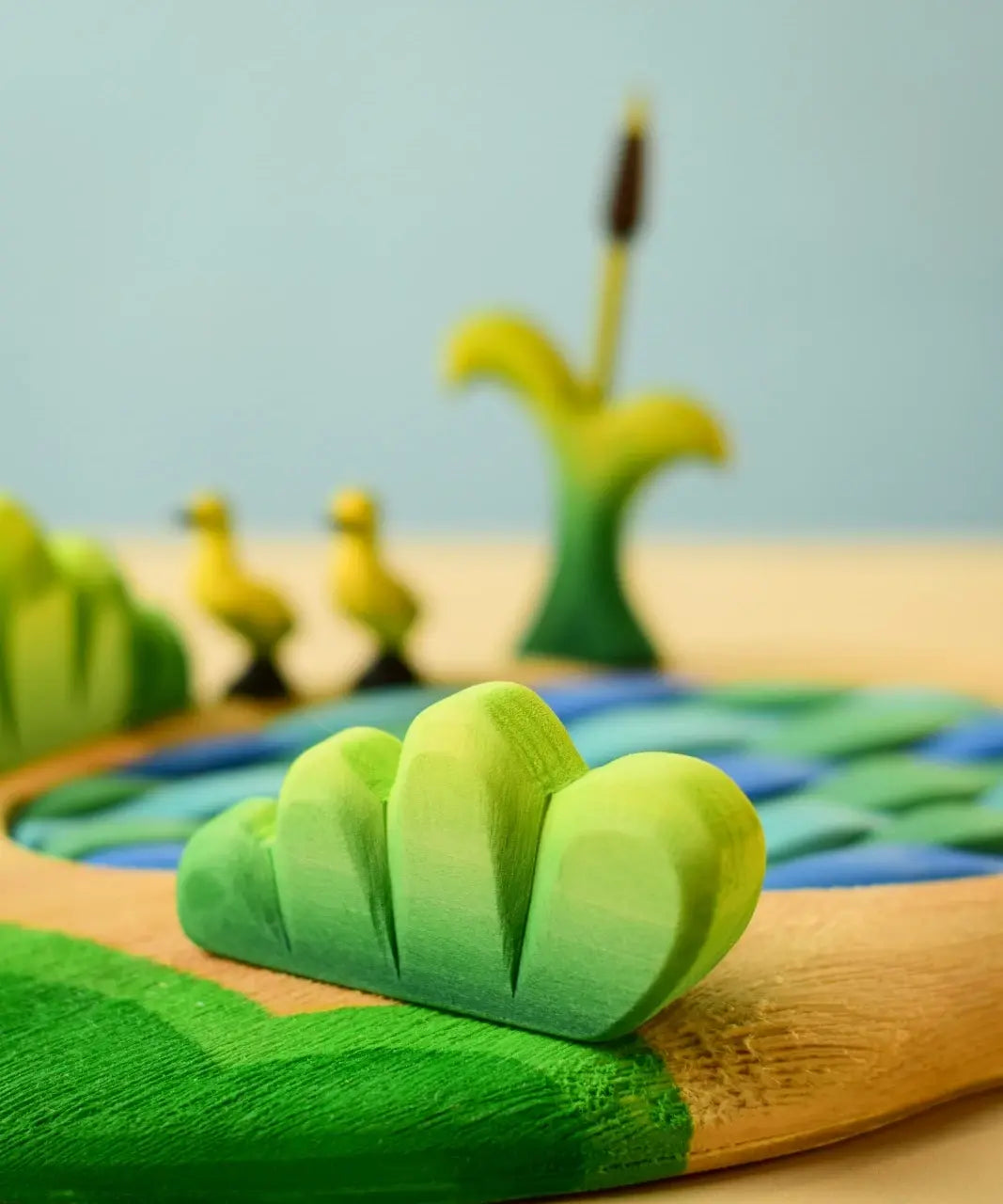 Bumbu Toys lake bush wooden toy scenery piece placed in a small world play scene with a lake and ducklings in the background.