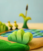 Bumbu Toys lake bush wooden toy scenery piece placed in a small world play scene with a lake and ducklings in the background.