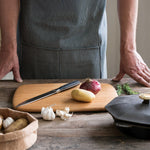 An adult standing over a wooden surface with the Bambu serving and cutting bamboo boards with a kitchen knife, red onion and potato on top for scale