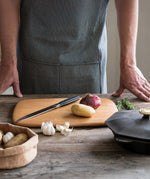 An adult standing over a wooden surface with the Bambu serving and cutting bamboo boards with a kitchen knife, red onion and potato on top for scale