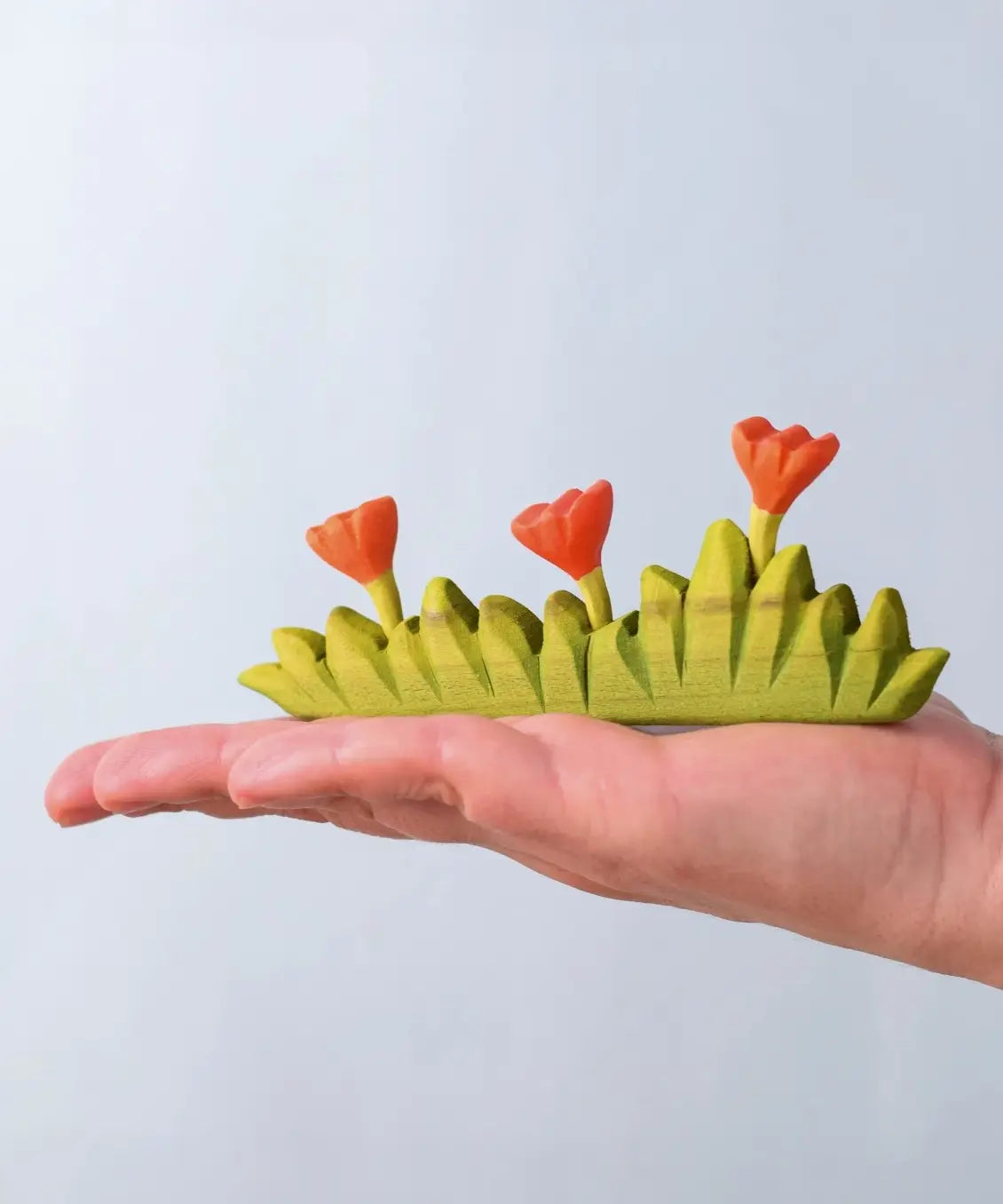Bumbu large grass with three orange flowers wooden toy scenery in an adult's hand.