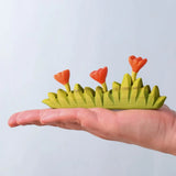 Bumbu large grass with three orange flowers wooden toy scenery in an adult's hand.