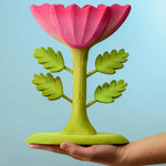 A person holding the Bumbu Wooden Large Pink Flower on their hand in front of a blue background.