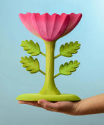 A person holding the Bumbu Wooden Large Pink Flower on their hand in front of a blue background.