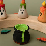 Bumbu handcrafted wooden black magic cauldron decorative figure in front of spooky candles on a celebration ring
