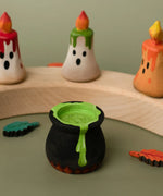 Bumbu handcrafted wooden black magic cauldron decorative figure in front of spooky candles on a celebration ring