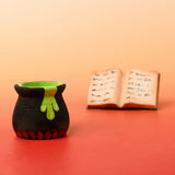 Bumbu handcrafted wooden black magic cauldron decorative figure in front of a spell book