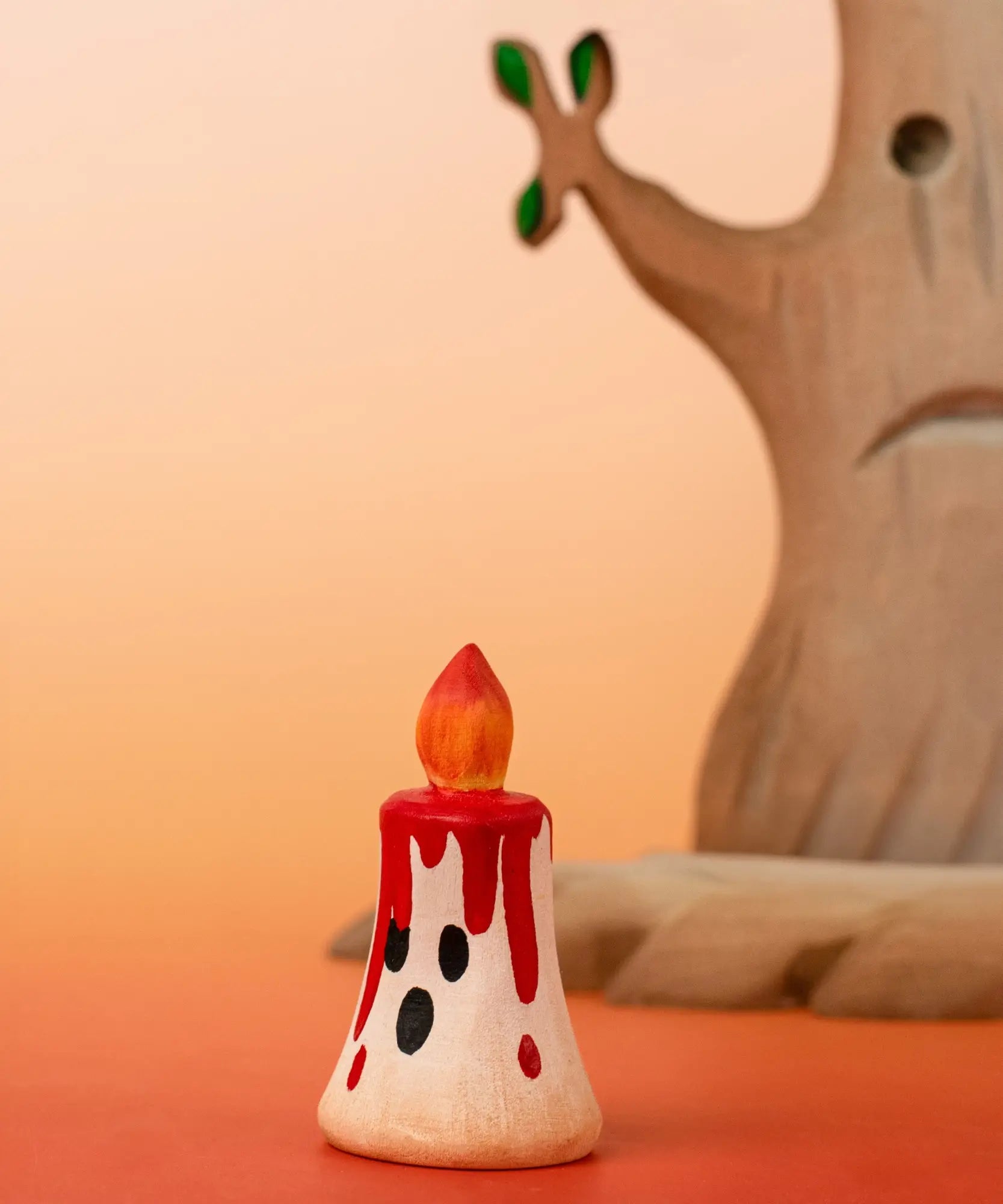 Bumbu handcrafted wooden magic red candle with a friendly face in front of a spooky tree figure