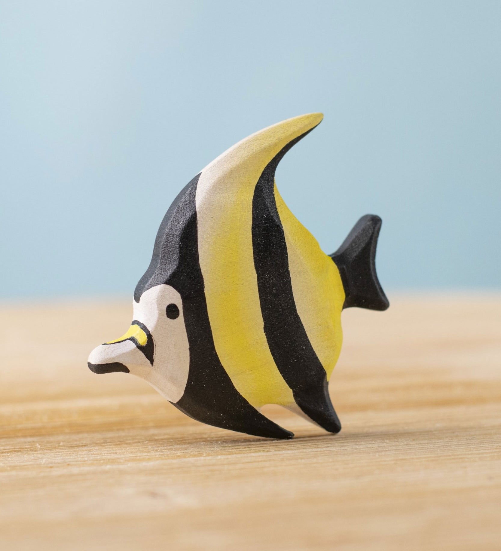 A Bumbu Toys Moorish Idol Fish handmade wooden figure placed on a wooden surface. The fish has a yellow and black striped detail.