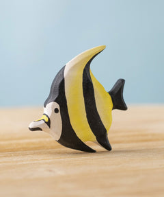 A Bumbu Toys Moorish Idol Fish handmade wooden figure placed on a wooden surface. The fish has a yellow and black striped detail.