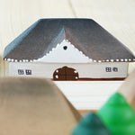 Close up of the Bumbu Muntenia handmade wooden house toy next to some grapat mandala trees