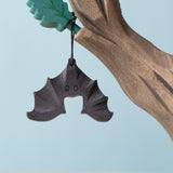 Bumbu handmade and hand painted wooden bat figure available at Babipur with its wings spread out. Features a small hole with a thread looping through for the bat to hang off a tree