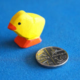 Bumbu eco-friendly wooden chick figure on a blue background next to a 5 pence coin