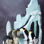 Ostheimer and Holztigher wooden penguin figures placed on a reflective surface with the Bumbu icy cliffs in the background